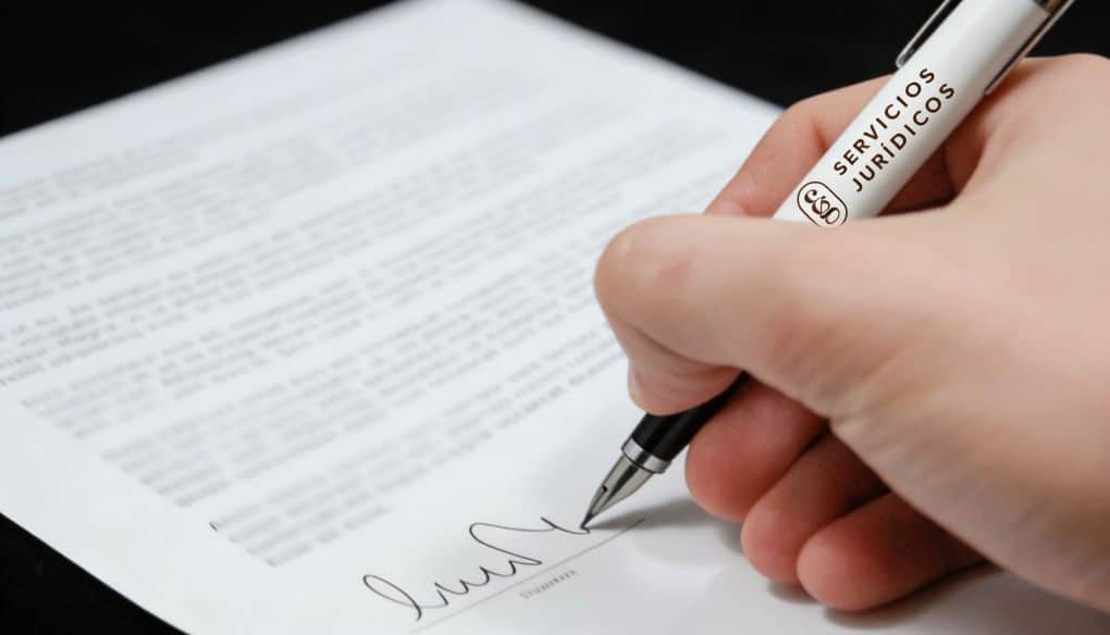 Una mano firmando un contrato sobre una mesa